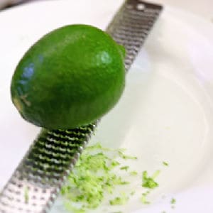 A lime on a microplane being grated into a bowl.