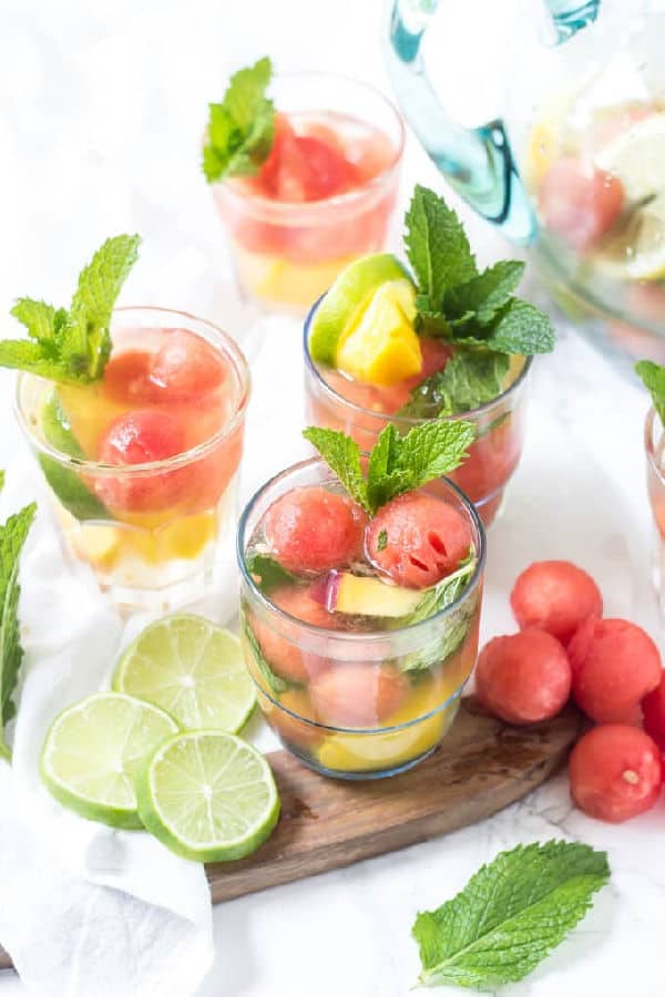 Four cocktails garnished with lime and watermelon balls.