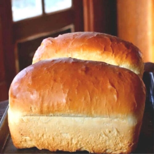 Two finished loaves of Amish white bread cooling on a table.