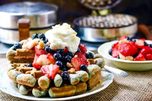 small stack of blue cornmeal waffles with whipped cream and berries on top.