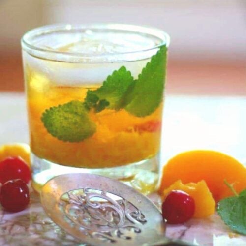 A peach bourbon mule in an on the rocks glass garnished with mint