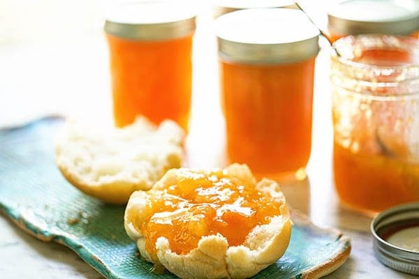 Sweet apricot jam on biscuit with jars of jam.