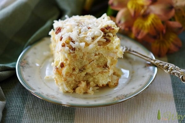 Yellow cake topped with coconut and pecans with silver fork on green and gold floral edged china plate.