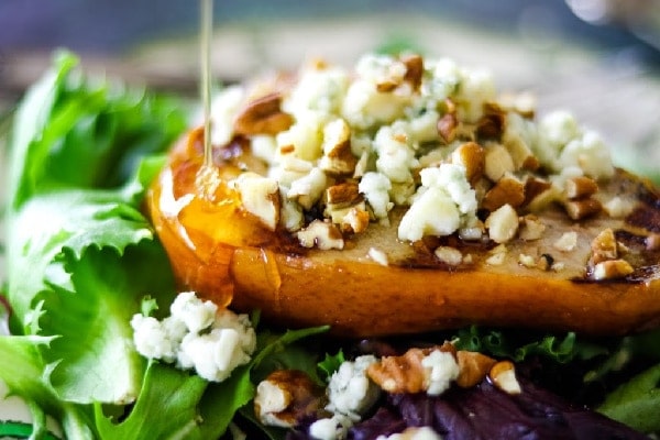 A grilled pear is being drizzled with honey.