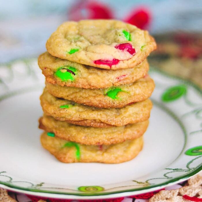 stack of m&ms cookies with red and green candies on a white plate with green trim.