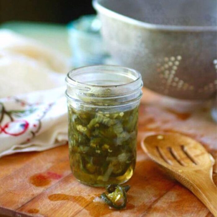 A glass jar of candied jalapenos on a wooden surface.