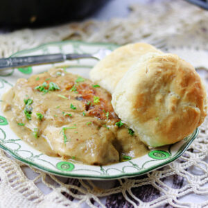 Smothered chicken and gravy on a plate with biscuits.