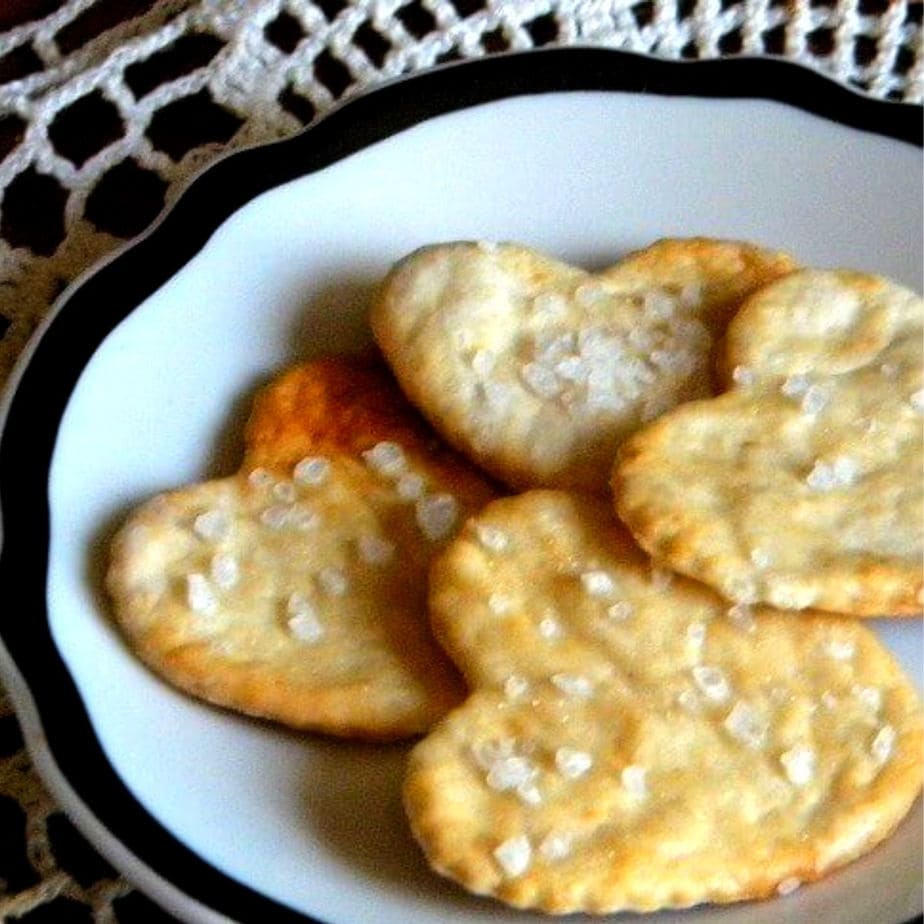 Homemade saltine crackers in hartvorm gesneden op een zwart-wit bord.