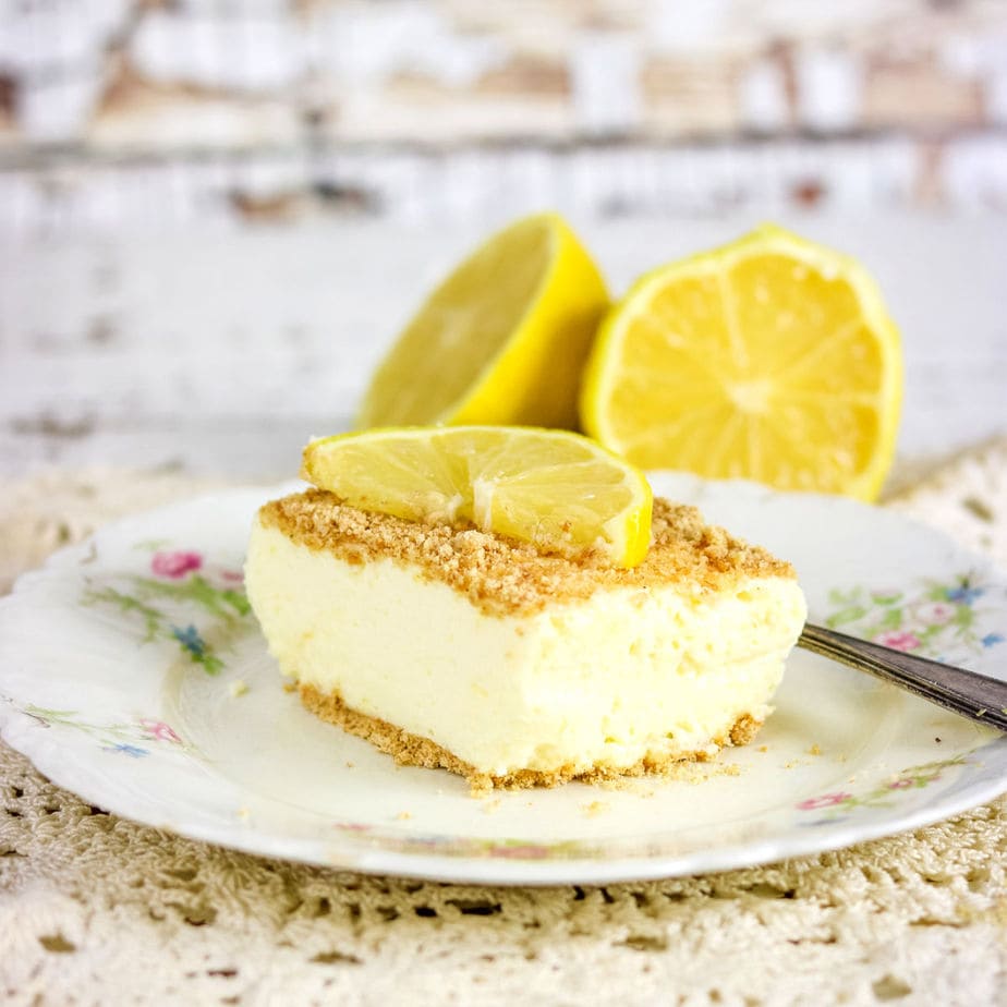A square of lemon cheesecake on a flowered plate with a lemon slice on top.
