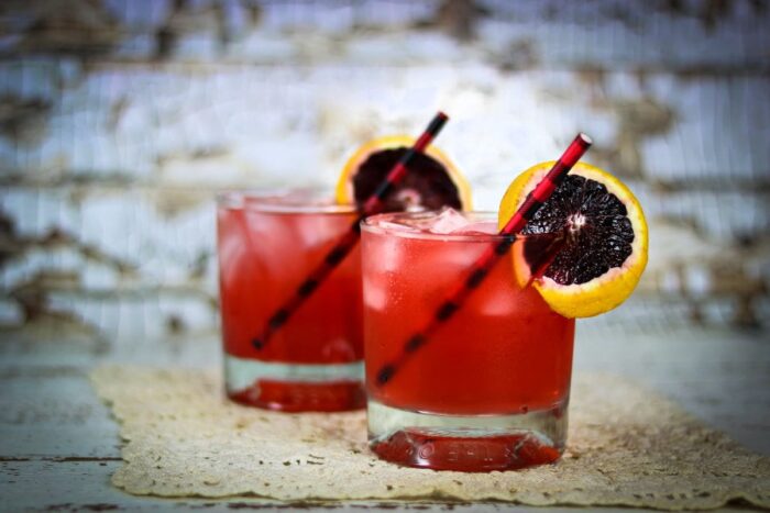 Two red cocktails in on the rocks glasses garnished with blood orange slices.