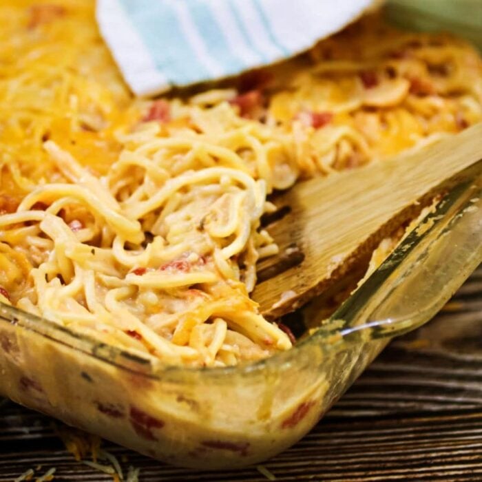 Chicken spaghetti in a casserole dish with a wooden spoon in it.