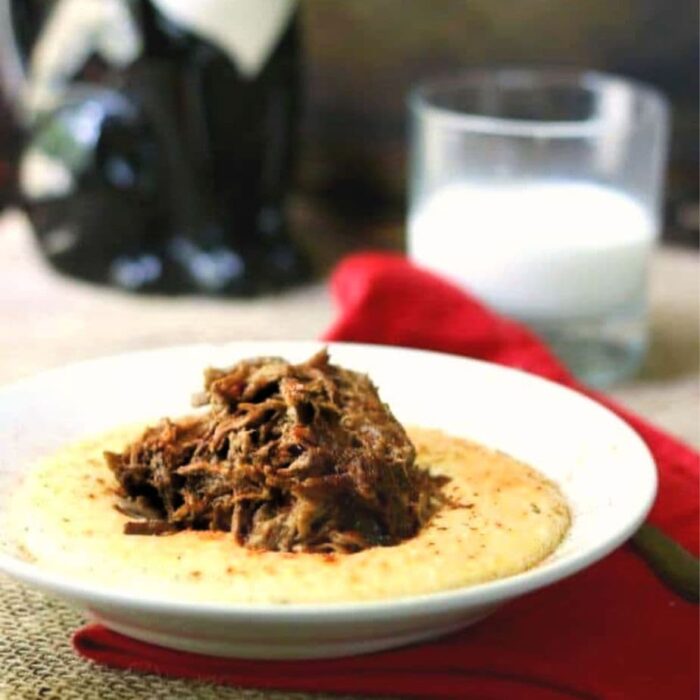 Close up of a bowl of cheese grits with pot roast spooned on top.