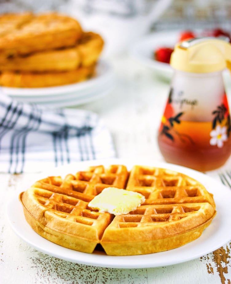 A finished waffle on a pate with a stack of waffles in the background.