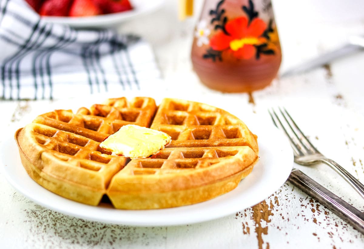 A plate of waffles with strawberries and syrup.