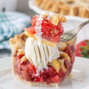 A slice of strawberry rhubarb pie with vanilla ice cream melting on top.