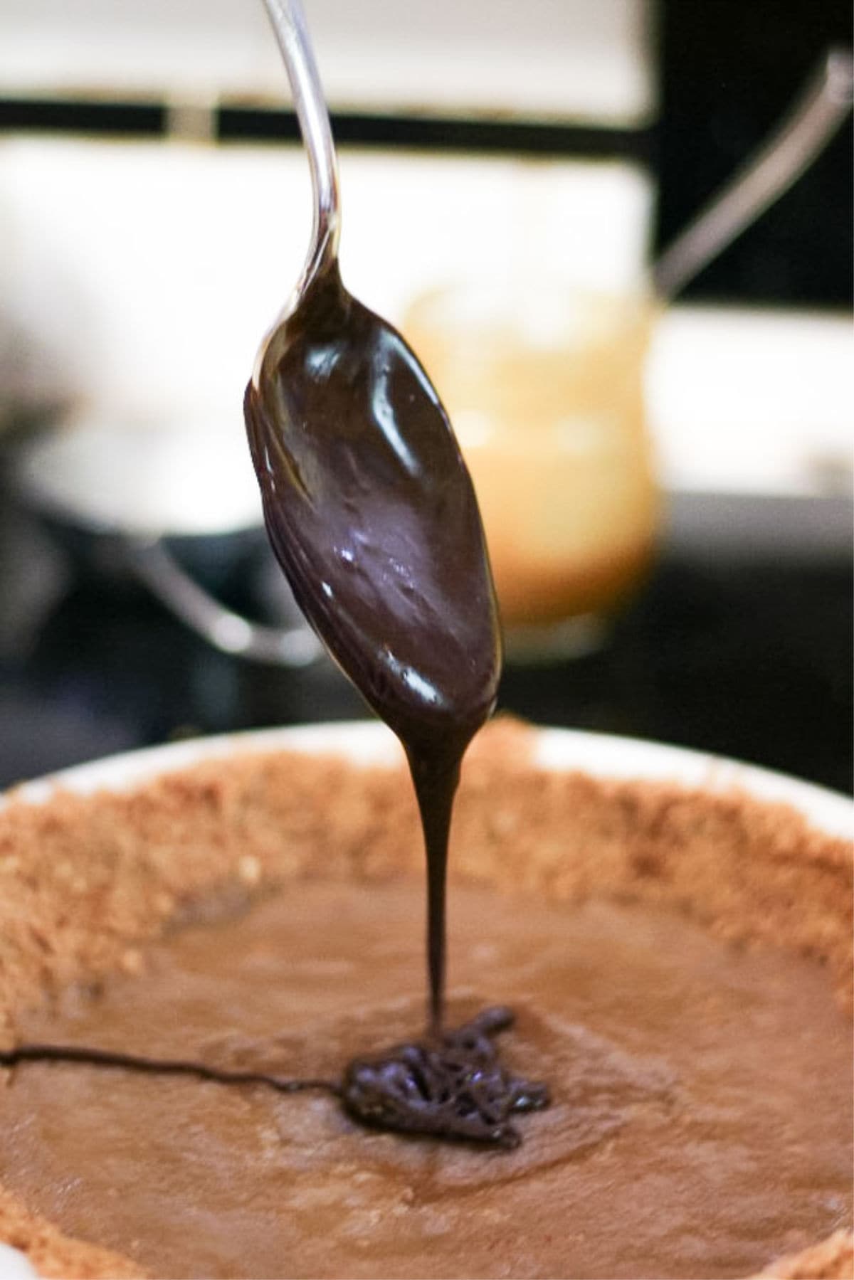 Melted chocolate ganache being spooned into a pie crust.