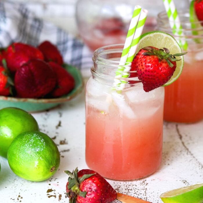 A pink cocktail in a Mason jar with green and white striped straws. Square image for feature and recipe card.