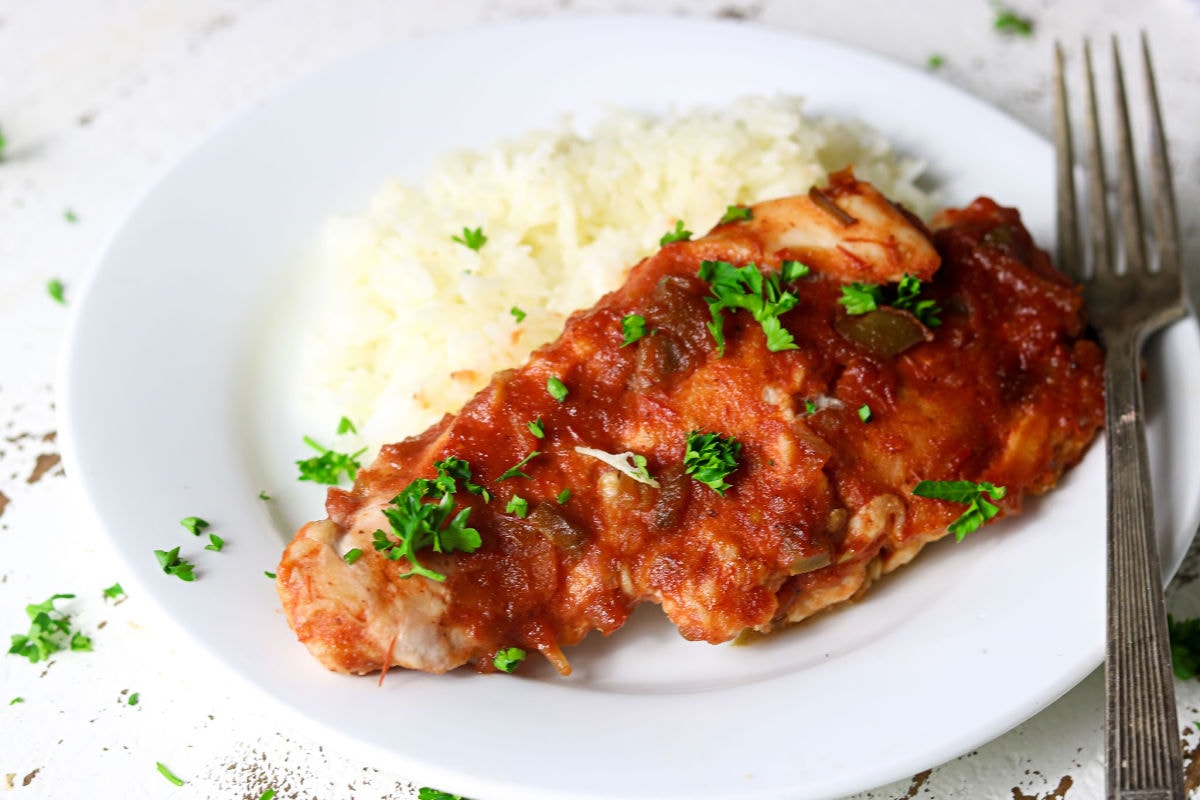 Closeup of the chicken covered in red sauce on a plate.
