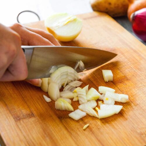 Knife chopping onions on a chopping board.