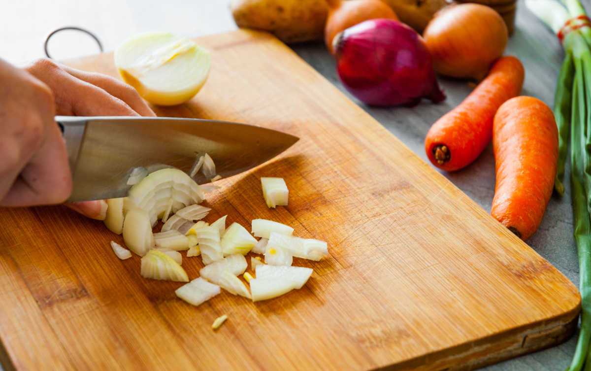 Onions being chopped on a wooded board.