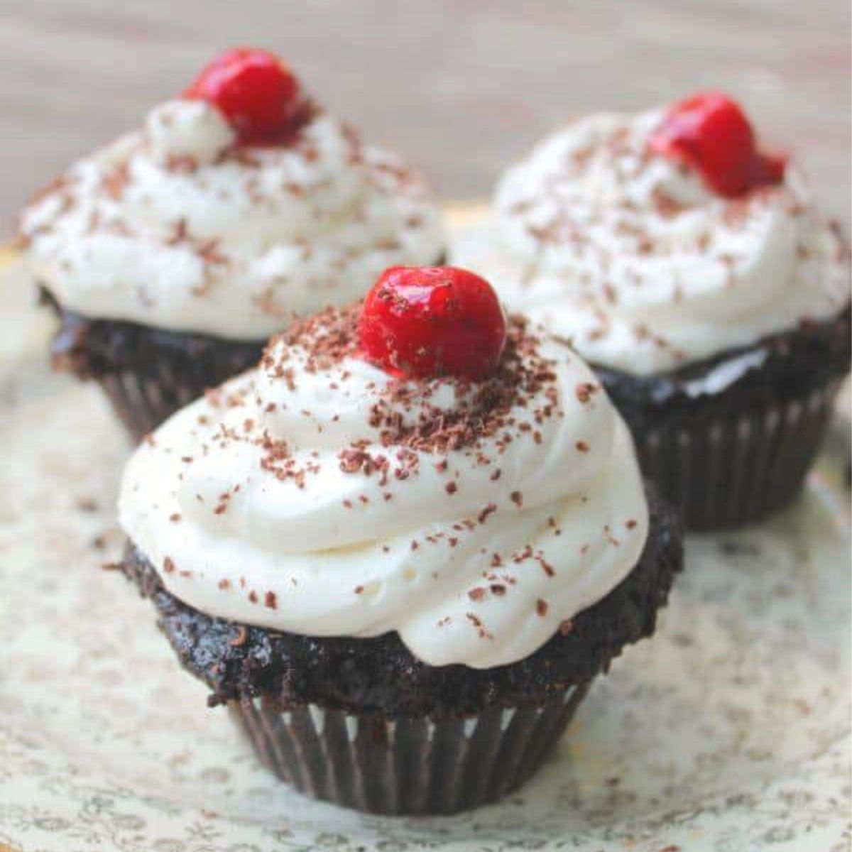 Three chocolate cupcakes with white icing and a cherry on top.