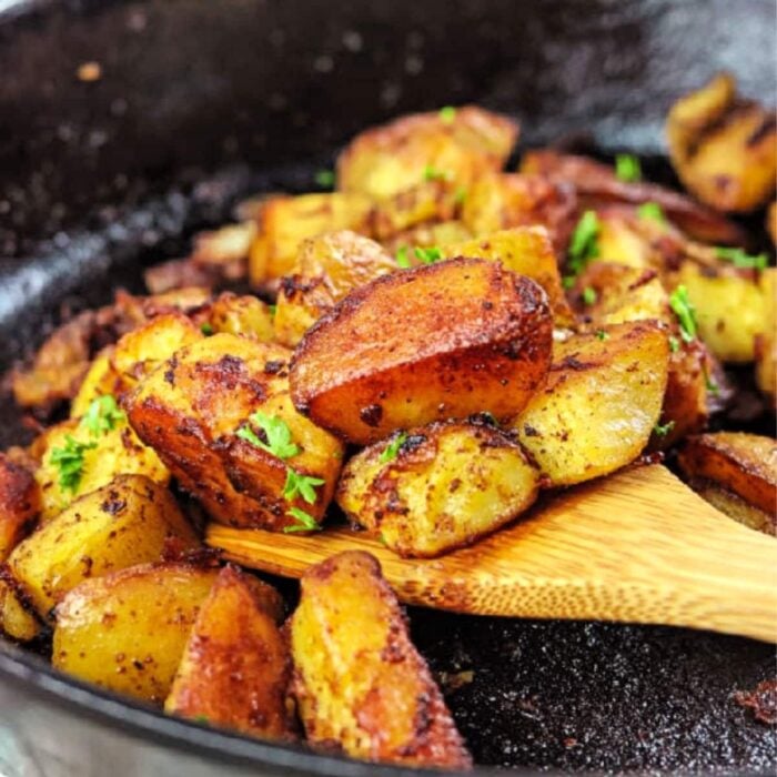 Wooden spatula removing fried potatoes out of iron skillet.