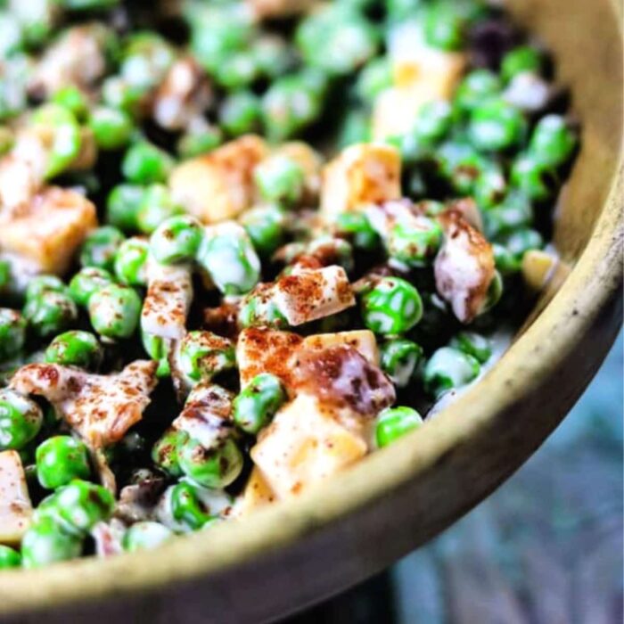 Peas and squares of cheddar cheese with a light dressing served in a bowl.