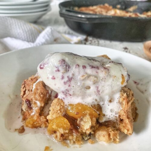 Closeup of a serving of peach dump cake with melting ice cream on top.