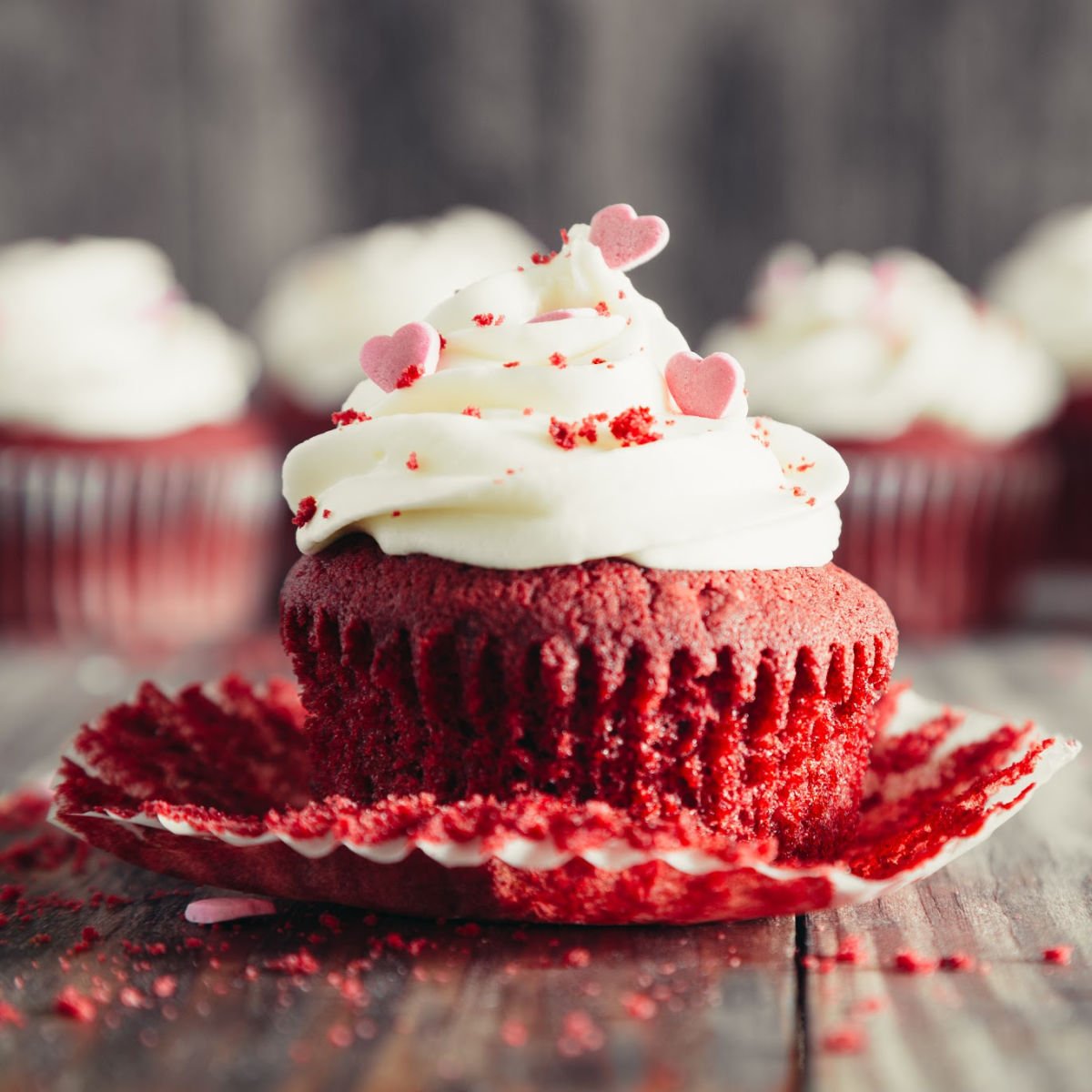 Red velvet cupcake with white icing and heart sprinkles.