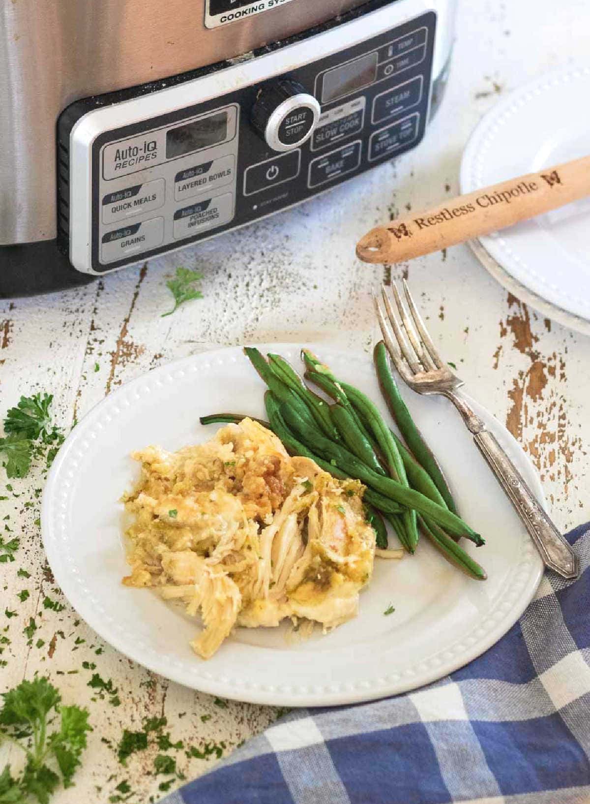 A serving of the recipe on a white plate with a slow cooker in the background.