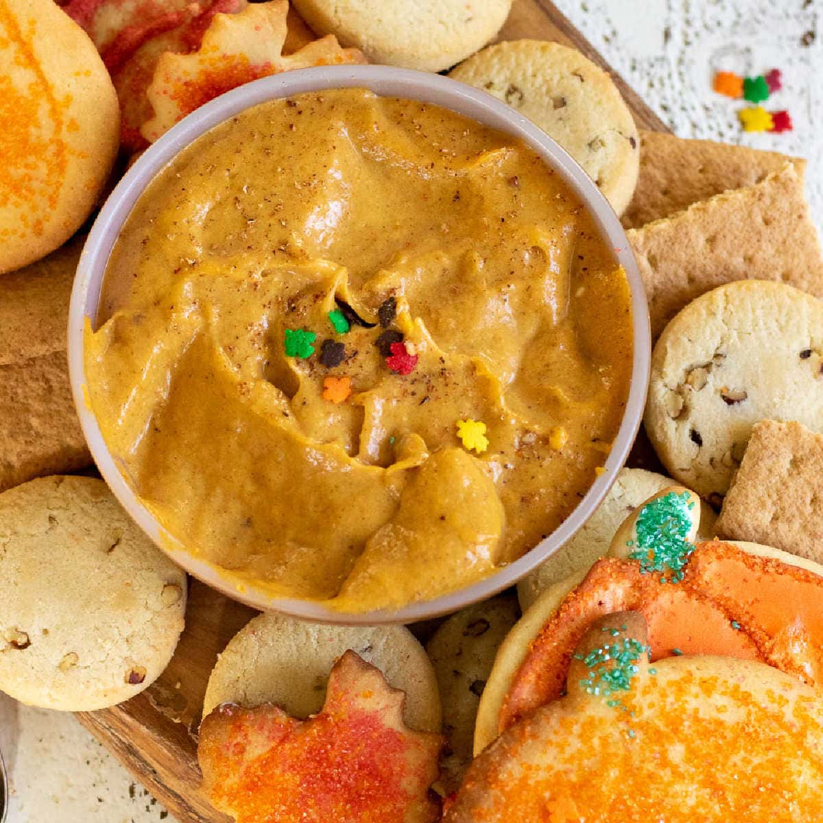 Close up of a bowl of pumpkin dip surrounded by cookies.