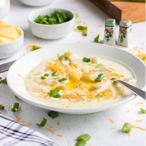 A closeup of potato soup in a white bowl garnished with butter.