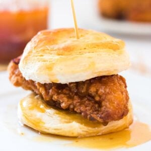 Close up of a biscuit with fried chicken on it and melted honey butter dripping from it.