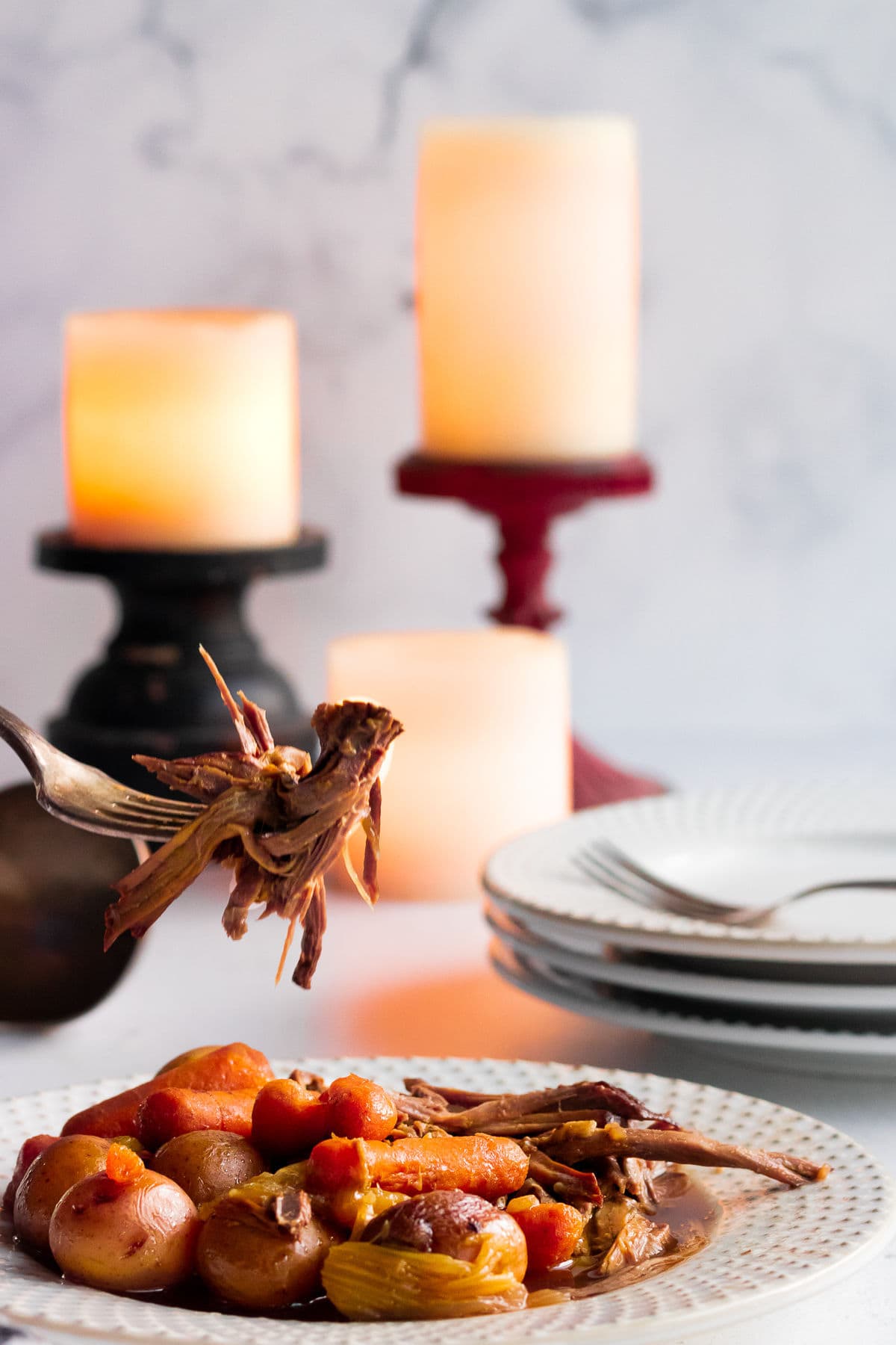 Forkful of beef roast with candles in the background.