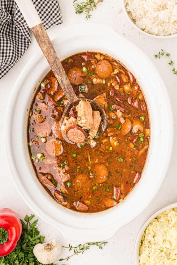 Overhead image of crock pot with chicken and sausage Gumbo with a spoon dishing it out.