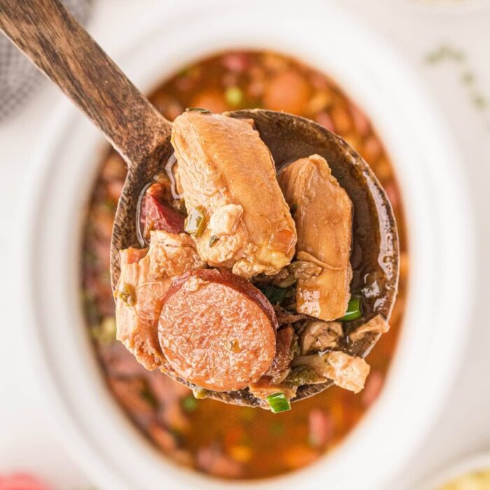 A spoon with chicken and sausage served from a crock pot filled with Gumbo