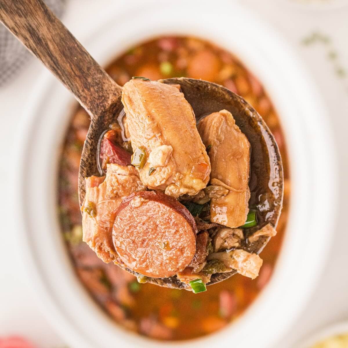 Chicken and sausage on a serving spoon from a slow cooker filled with gumbo.