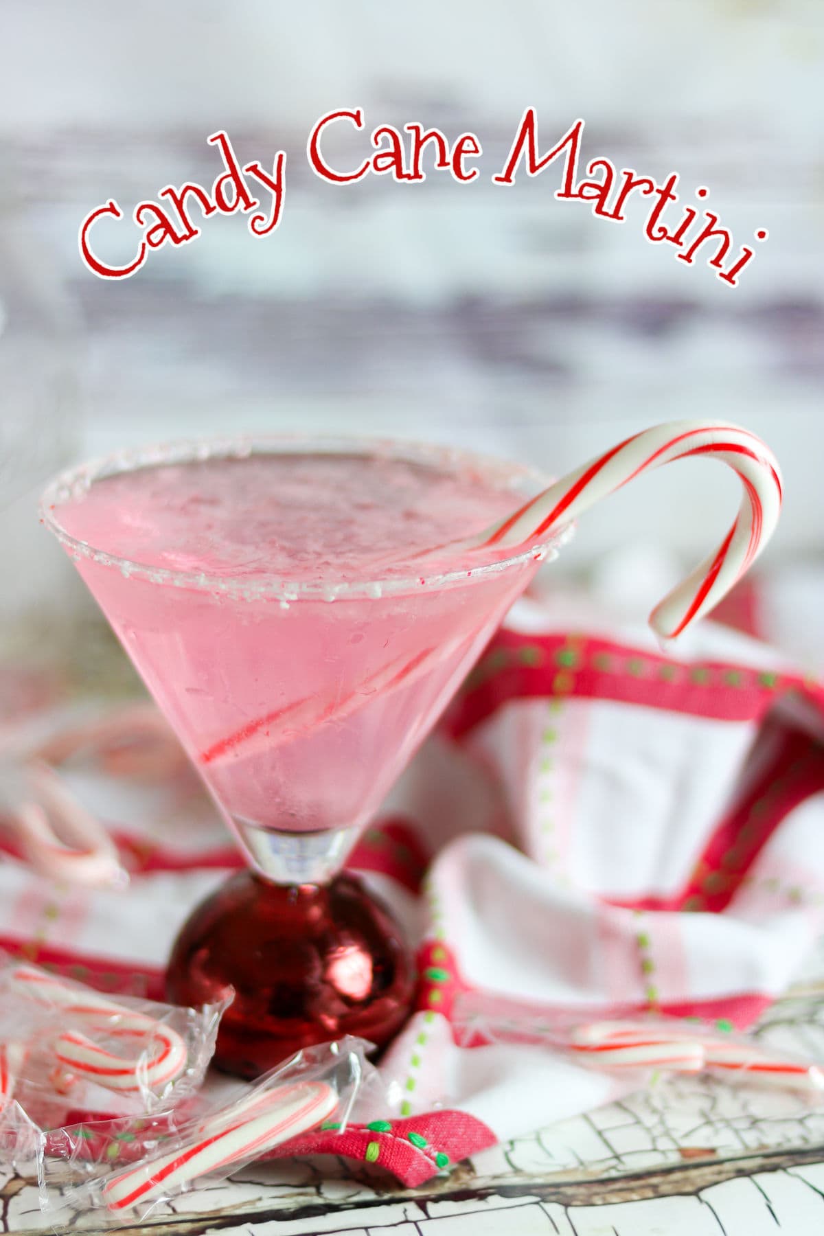 A pink candy cane martini in a glass with a peppermint stick garnish. Title text overlay.