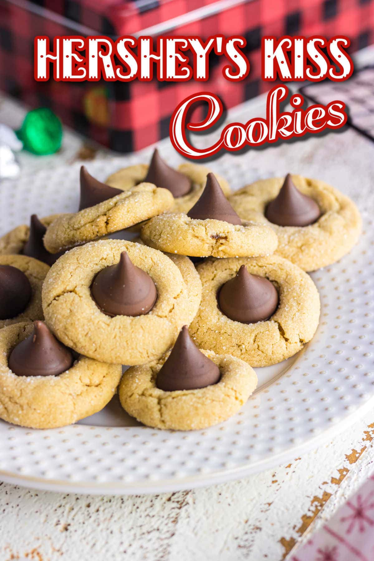 A peanut butter blossoms recipe straight from your childhood, this Hershey's classic is soft and chewy just like you remember. This easy peanut butter cookie recipe goes together fast, freezes well, and is full of chocolate and peanut butter flavor. Includes variations and tips for freezing peanut butter kiss cookies. #cookiesrecipe #easychristmascookies #bestpeanutbuttercookies A stack of cookies on a white plate with title text overlay.