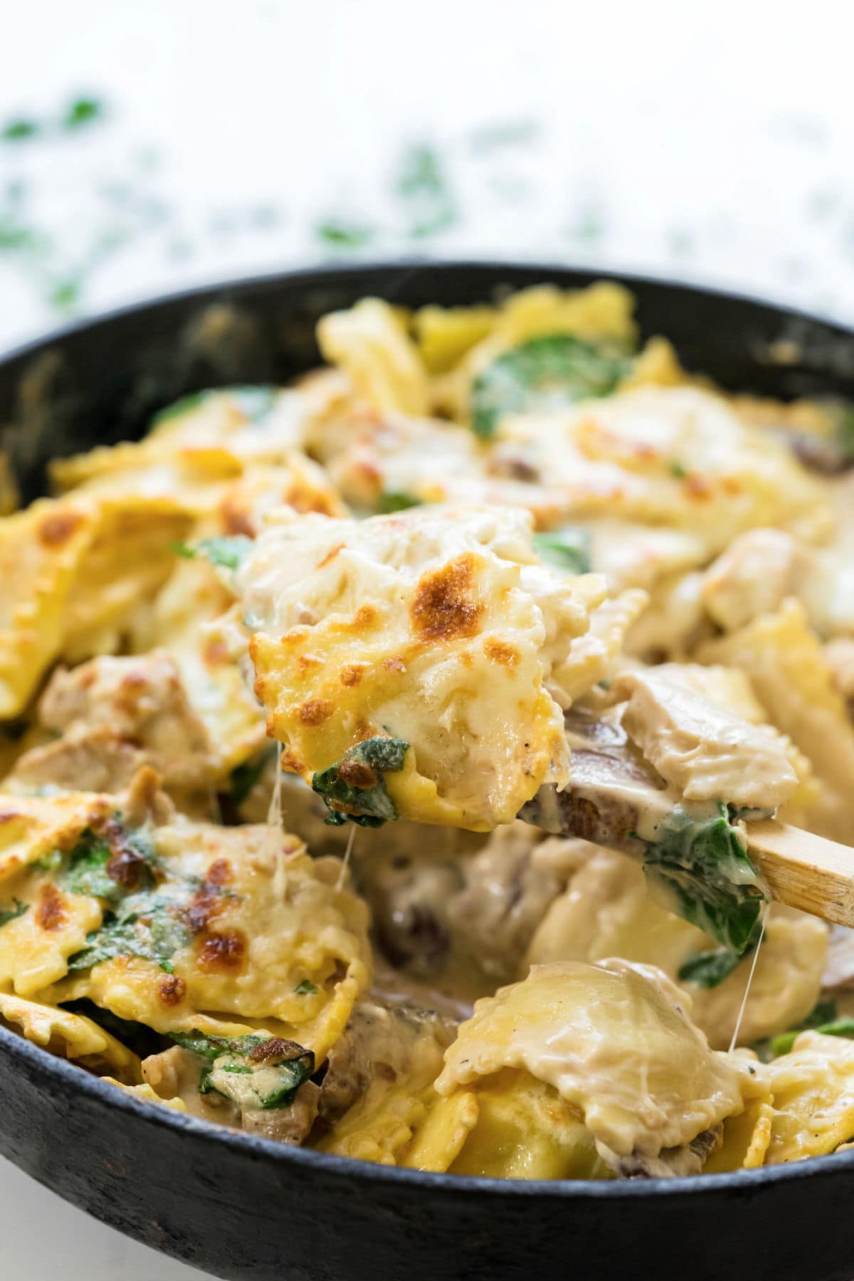 Finished chicken Alfredo ravioli in an iron skillet with a wooden spoon.