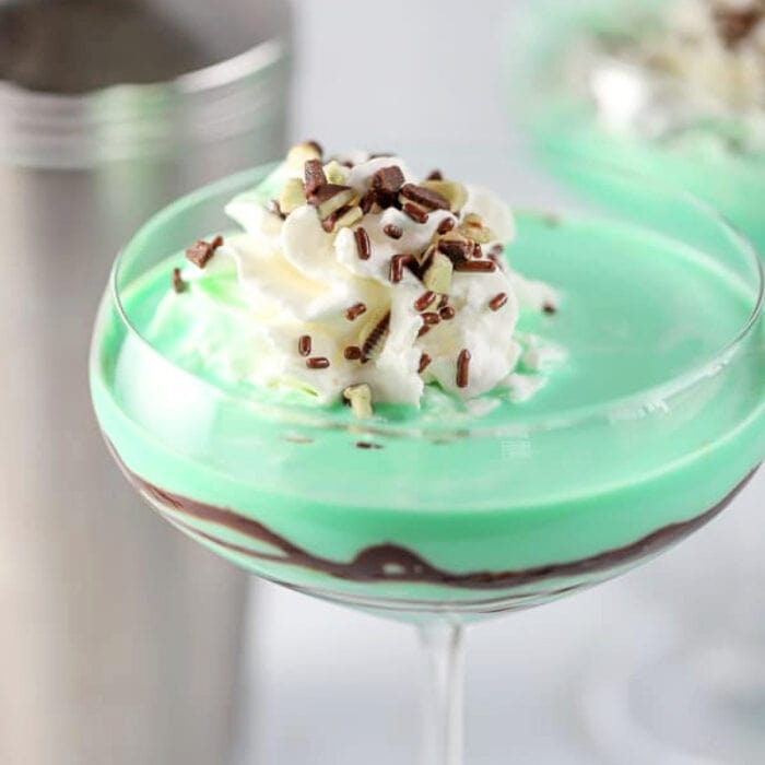 Close up of a green cocktail with a chocolate swirl garnished with whipped cream.