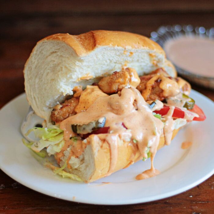Fried chicken sandwich made with French bread and dripping with sauce on a white plate.