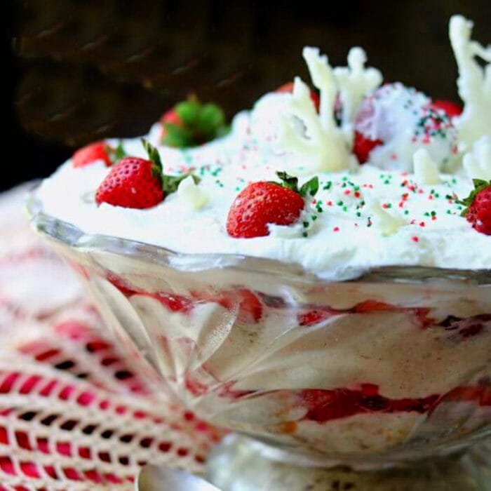 Layers of strawberries and cake in a punch bowl garnished with whipped cream on top.