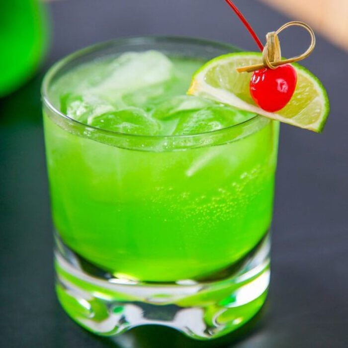 Green Midori Sour in an on the rocks glass garnished with a cherry.