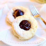 Close up of two raspberry thumbprint scones on a plate.