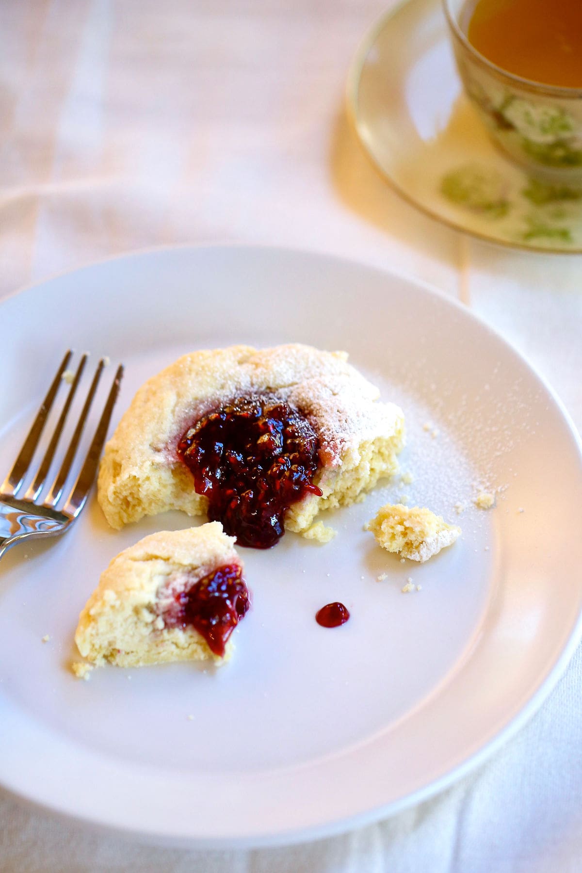 A half eaten scone on a plate with raspberry filling dripping off of it.