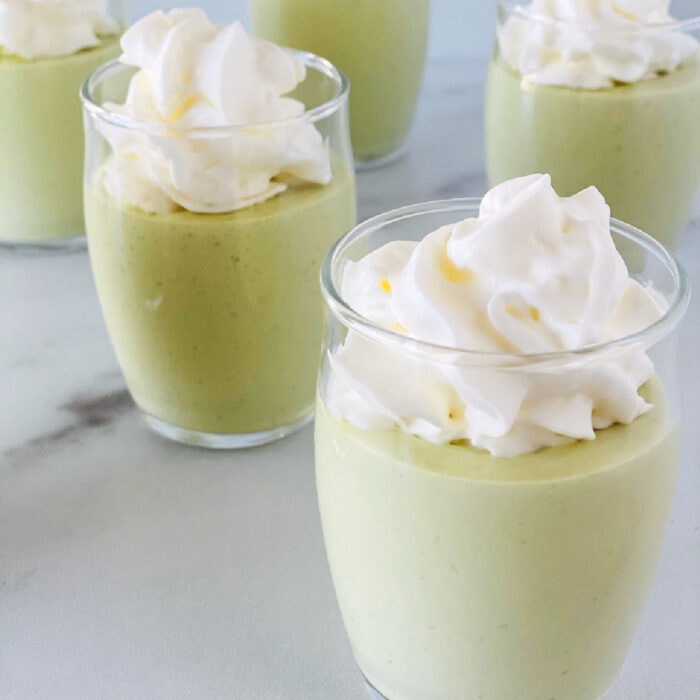 Light green pudding shots with whipped cream garnish.
