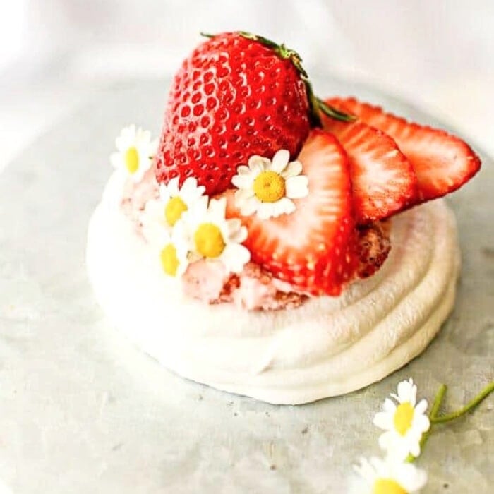 Close up view of a strawberry pavlova dessert decorated with chamomile flowers.