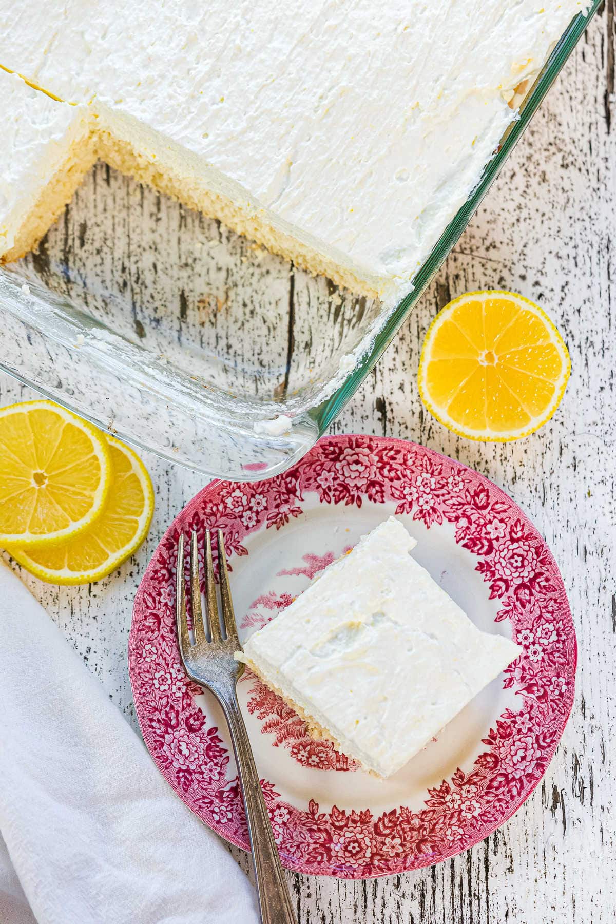 Overhead view of lemon cake on a plate with the pan of cake behind it.