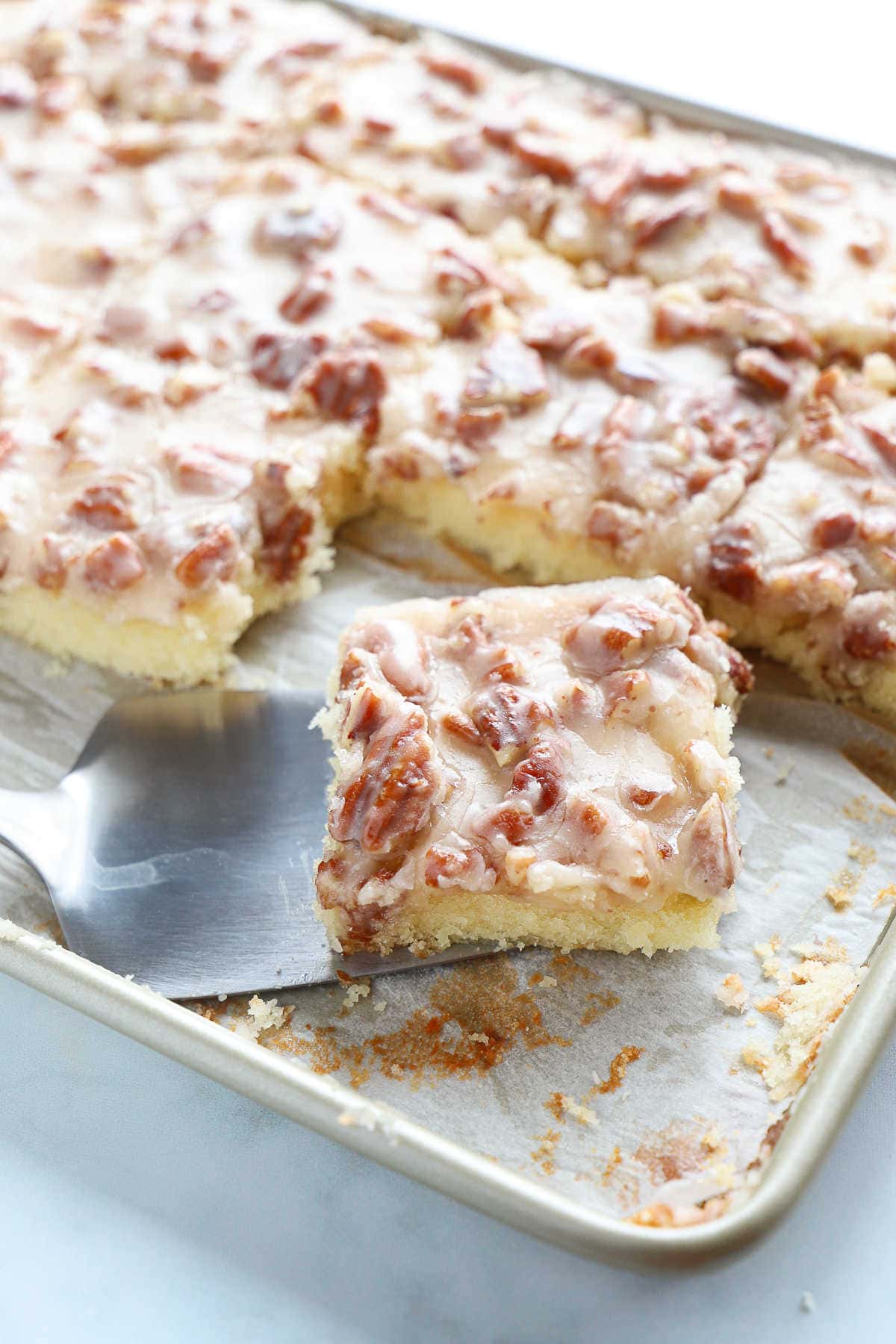 Vanilla sheet cake with a white fudge and pecan icing in a baking sheet.